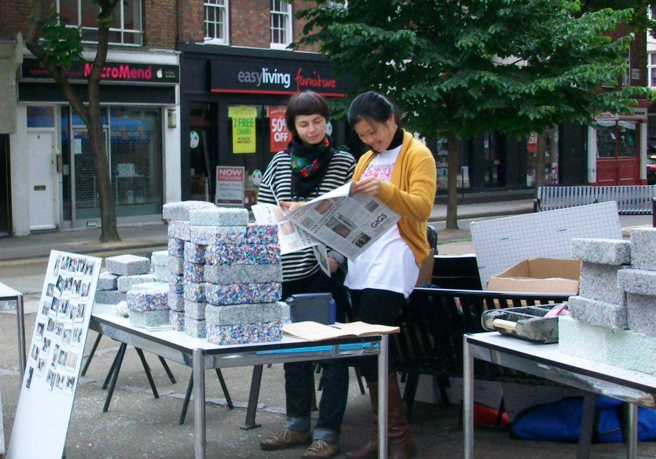 Two women read Fitzrovia News at a stall in Whitfield Gardens